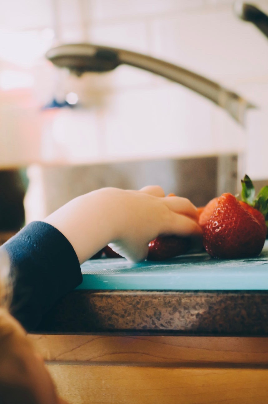 A child's hand grabbing a strawberry from a group of them on a counter.