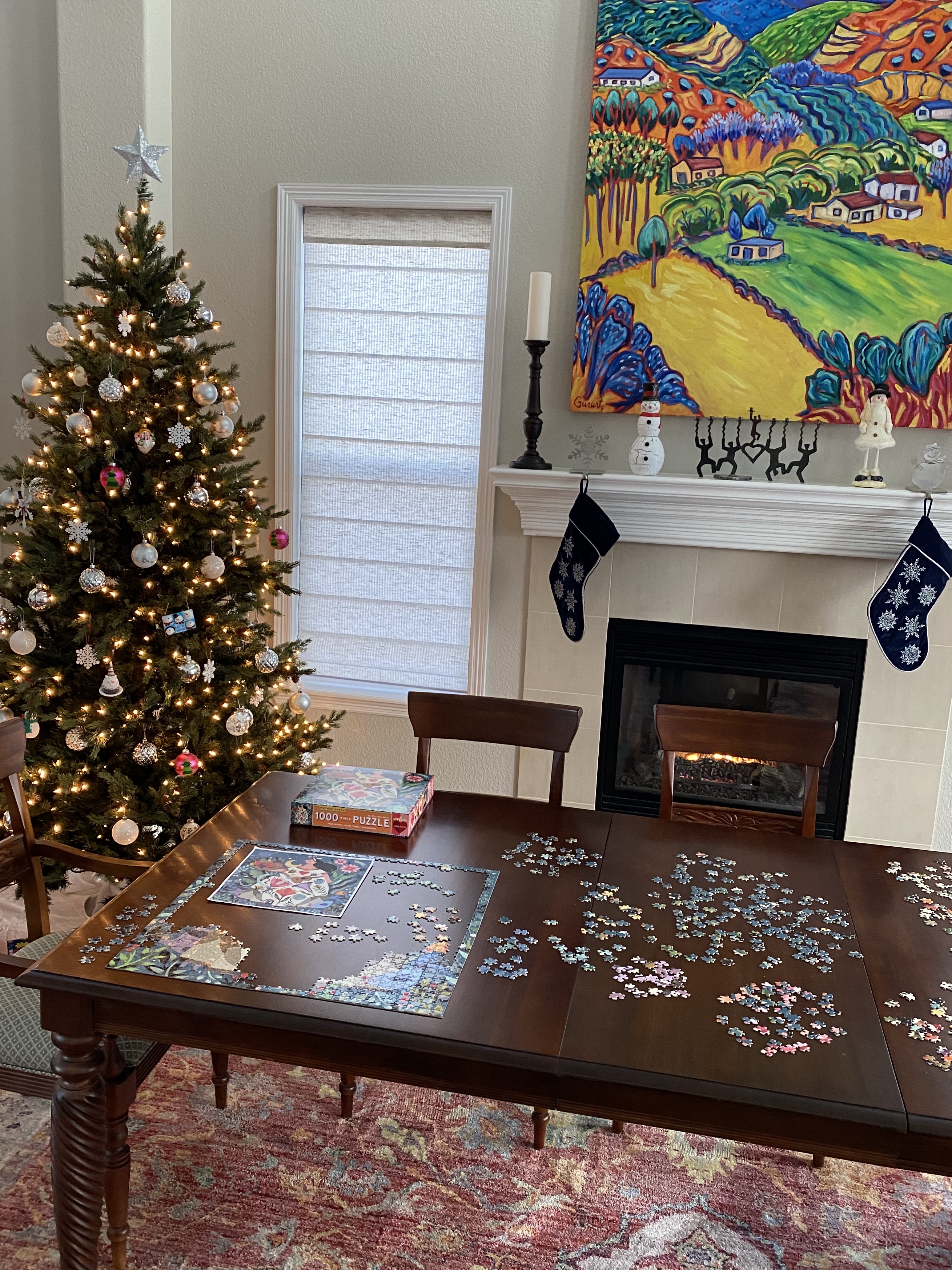 A room decorated with a Christmas tree, stockings on the fireplace, and other winter decorations, with a puzzle spread across a table.
