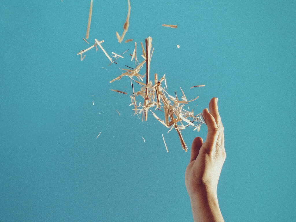 A hand throwing splinters of wood against a blue background.